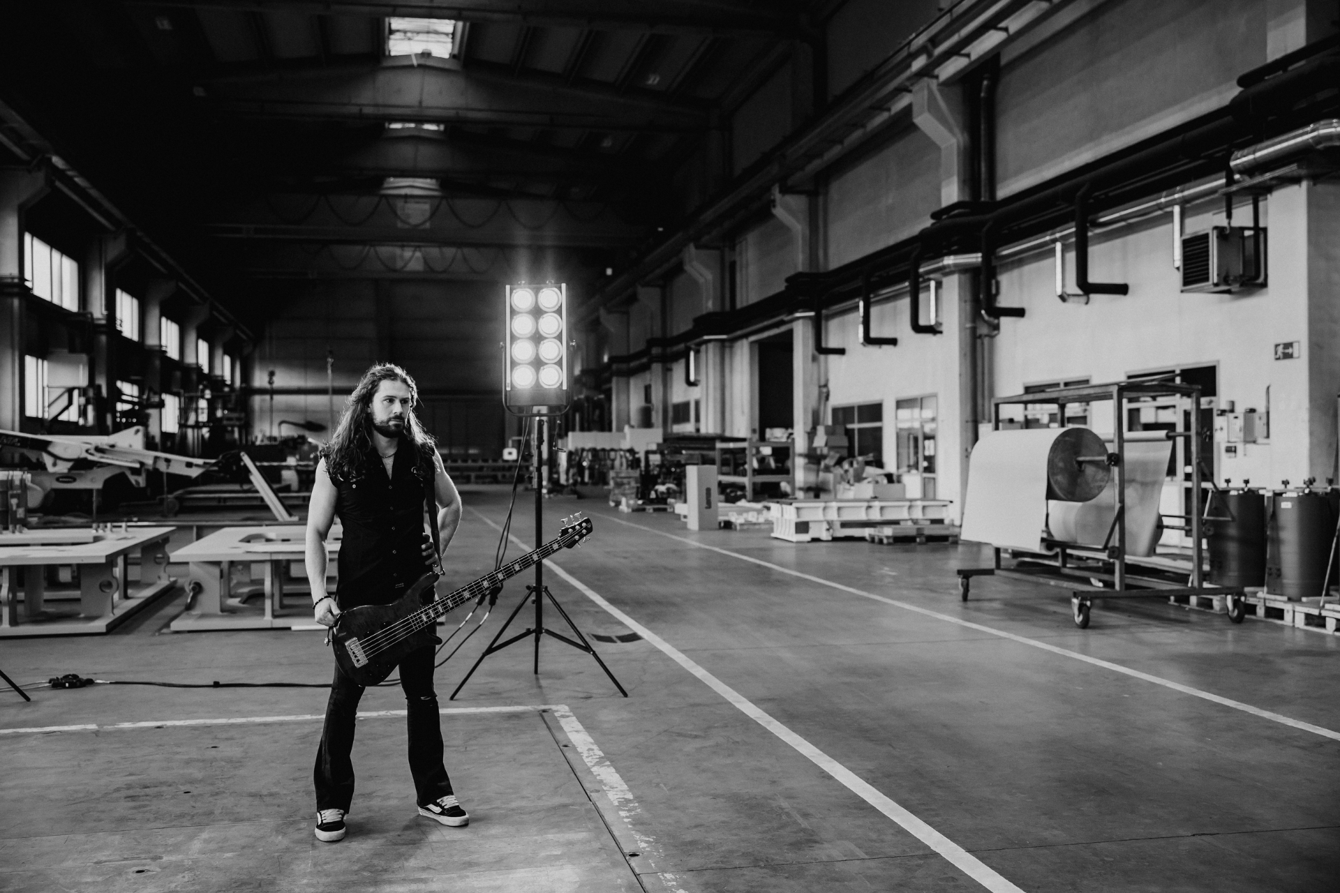 Luka standing with bass guitar in a black-and-white warehouse portrait.