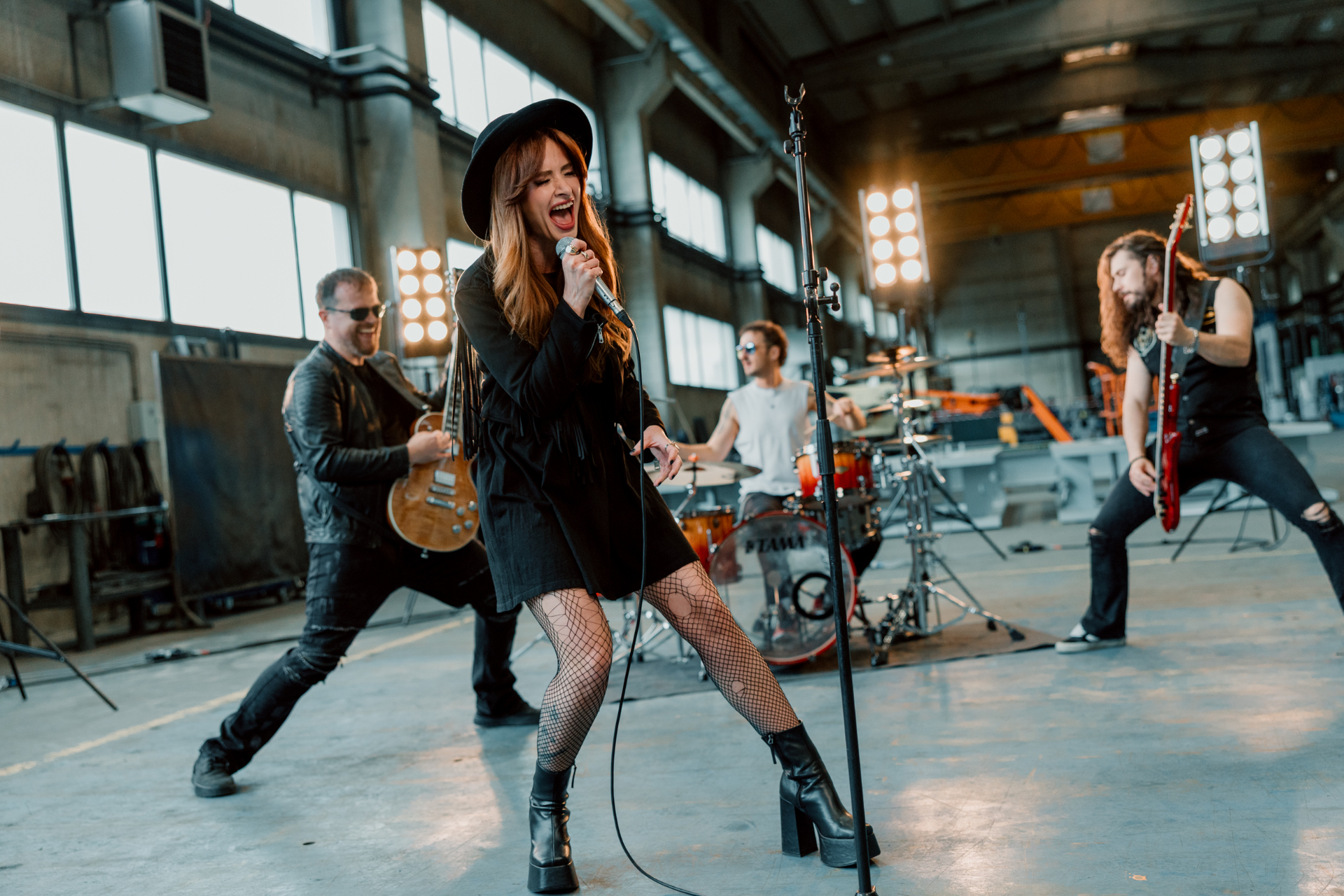 Kati singing at center stage with the full band performing in a warehouse location.